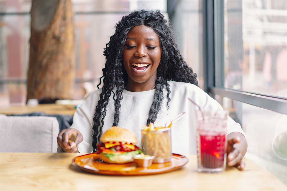 Black 25-year-old woman eating a burger and fries and drinking a soda in a re