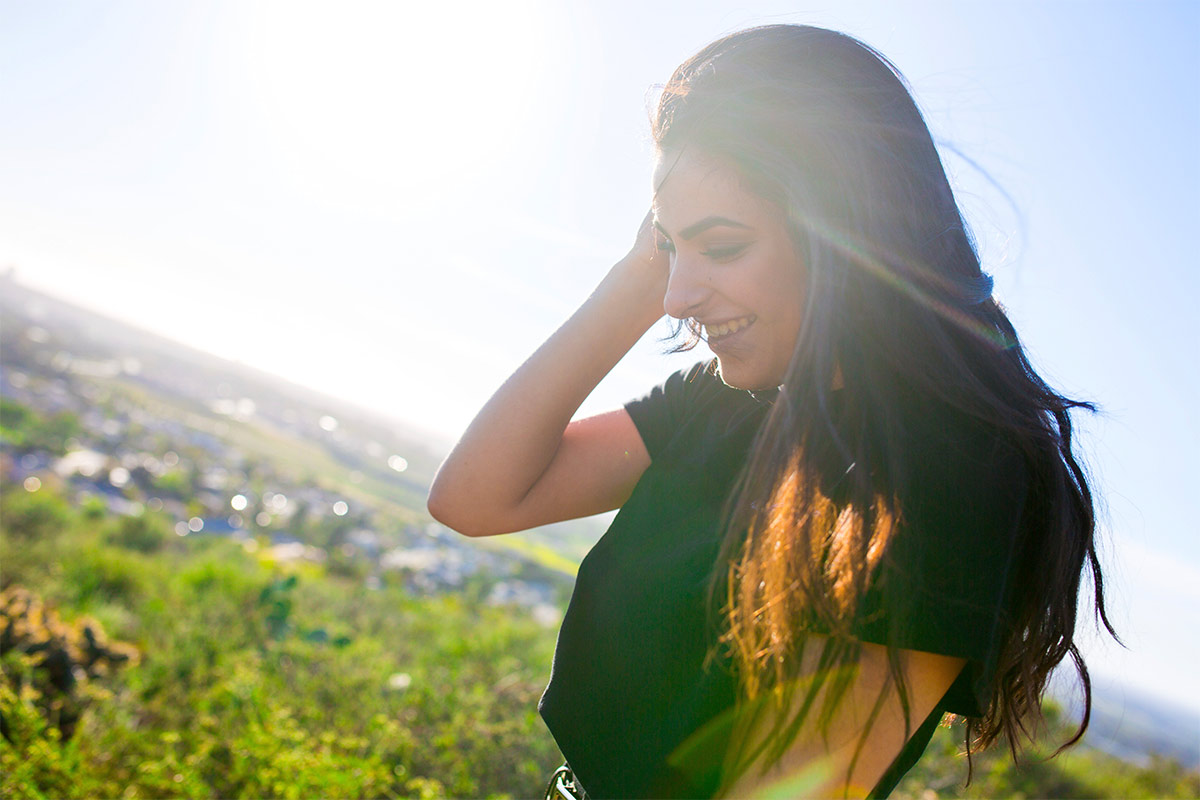 White 25-year-old woman smiling outside in the sunshine. 