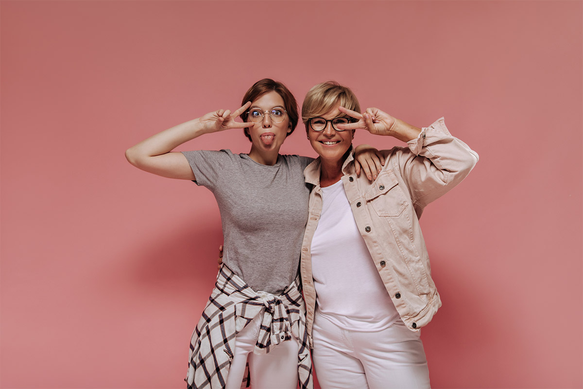  A 60-year-old white woman and a 28-year-old white woman sticking her tongue out pose holding peace signs in front of their faces.