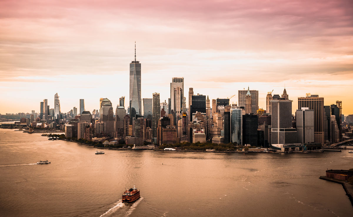 Horizon of New york city during sunset, with boats moving on the water next to the city. 