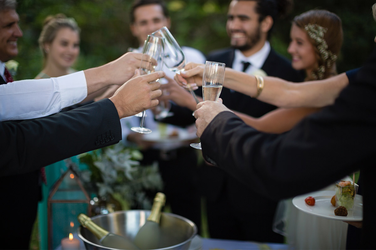 White people's hands at an outdoor event clinking glasses together in a circle