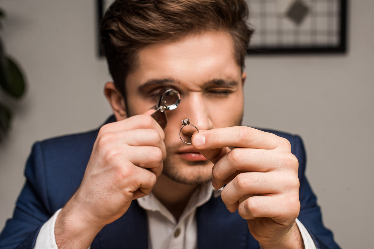 White professional man in his 30s examines diamond ring under magnifying glass tool 