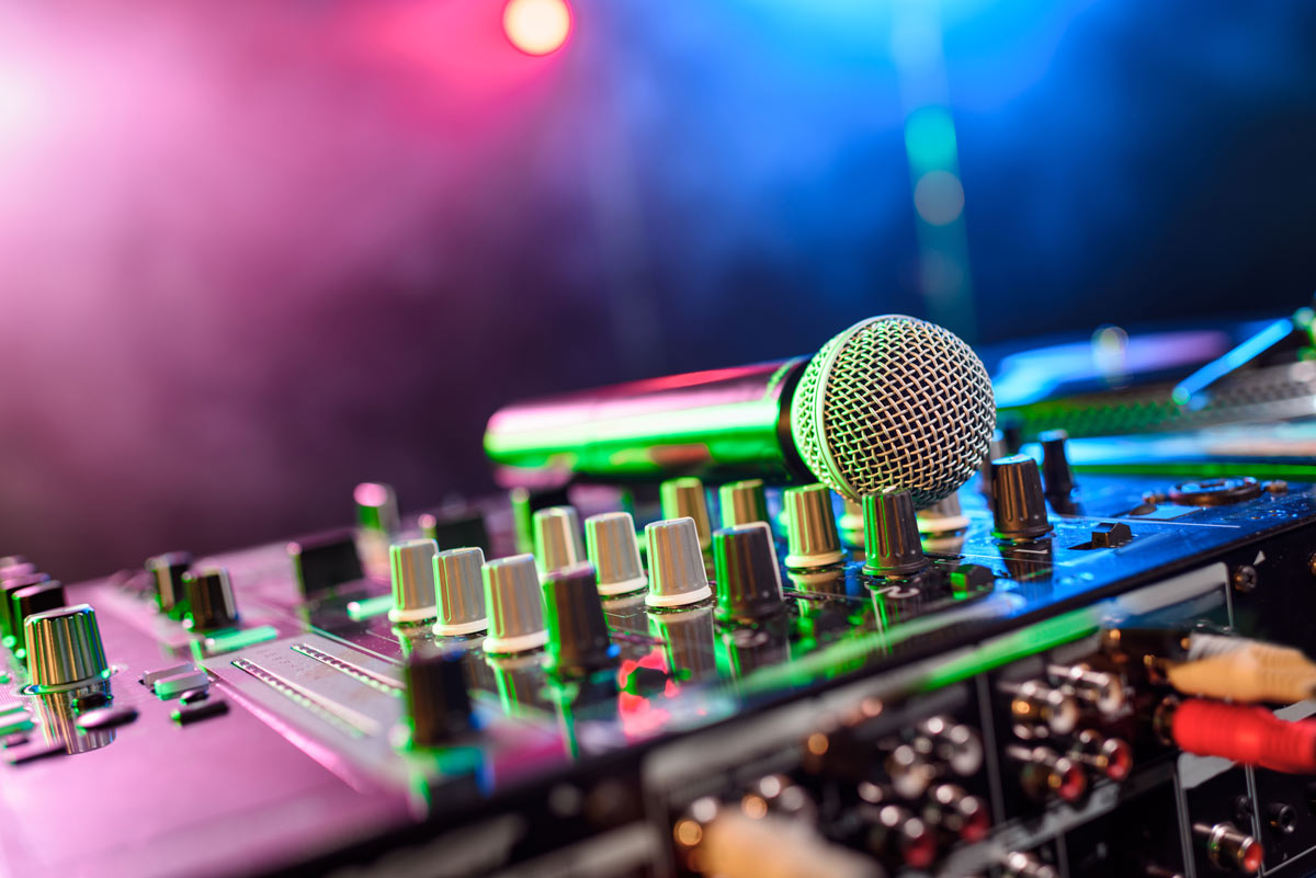 Microphone laying on a sound board that has pink and blue lights shining on it at a club. 