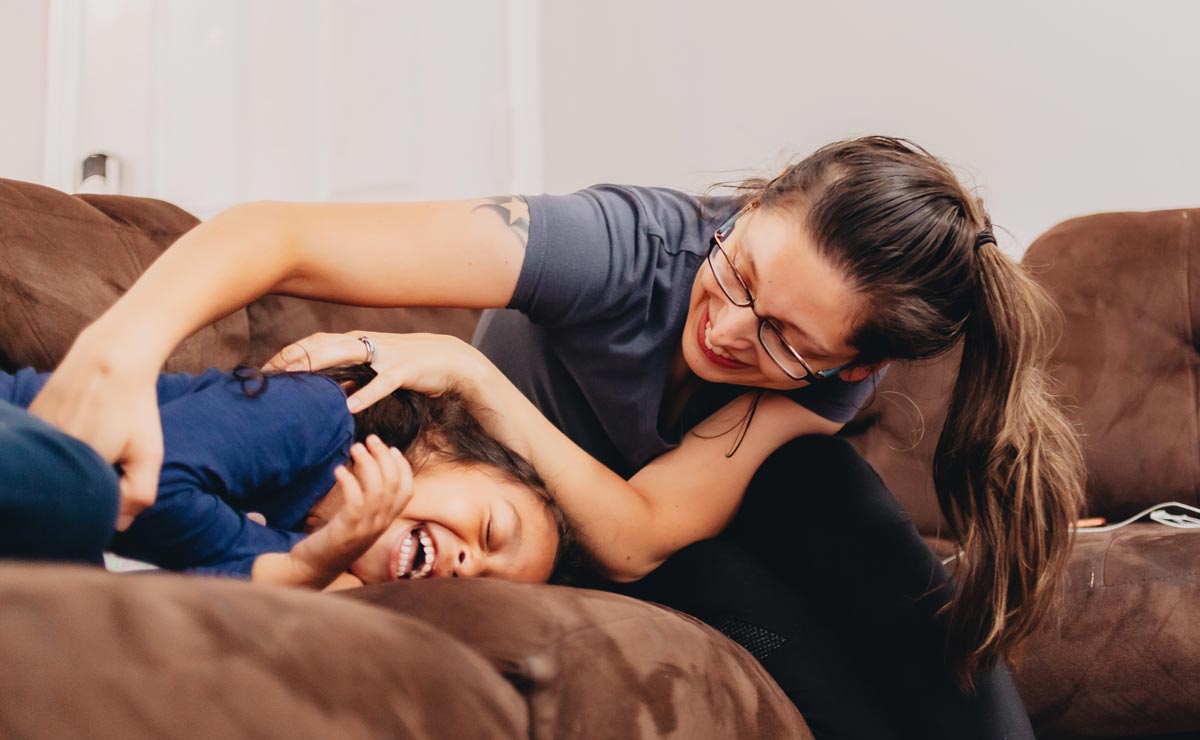 Two white little girls laughing and having a tickle fight on the couch 