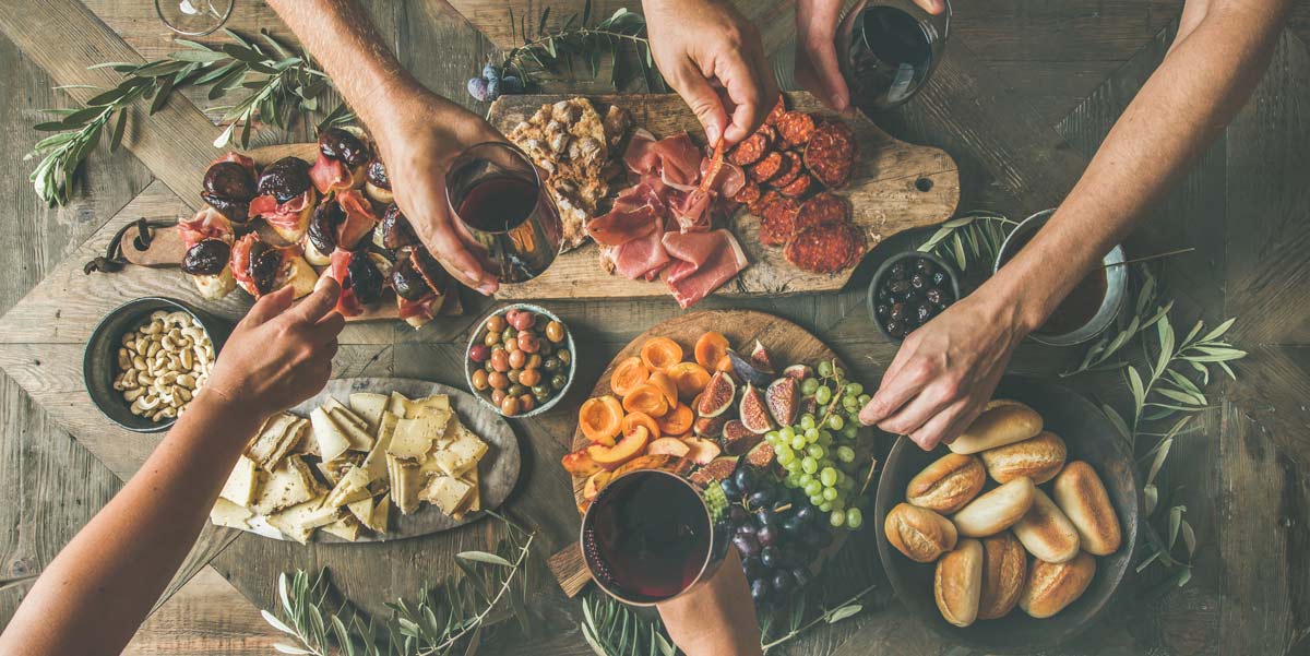 Hands holding wine and reaching for snacks upon a table of assorted charcuterie and snack boards