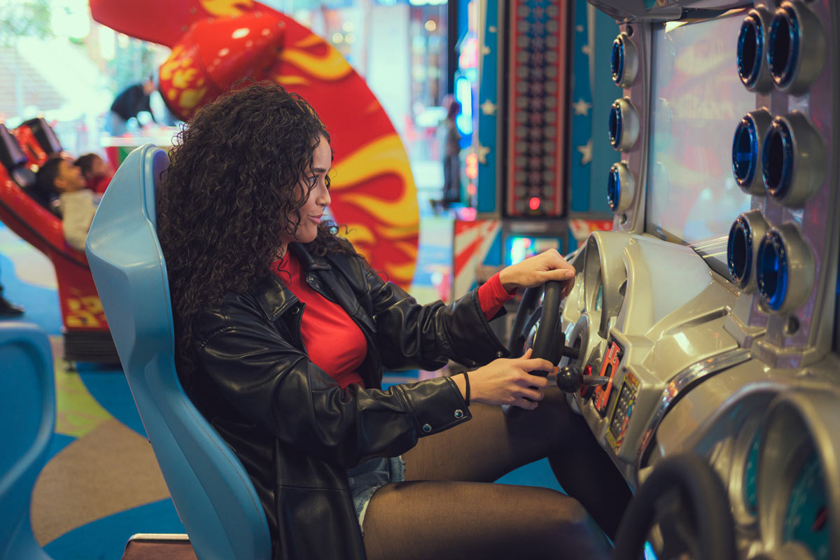 Hispanic 20 something women, sitting at a racing arcade game and steering a steering wheel. 