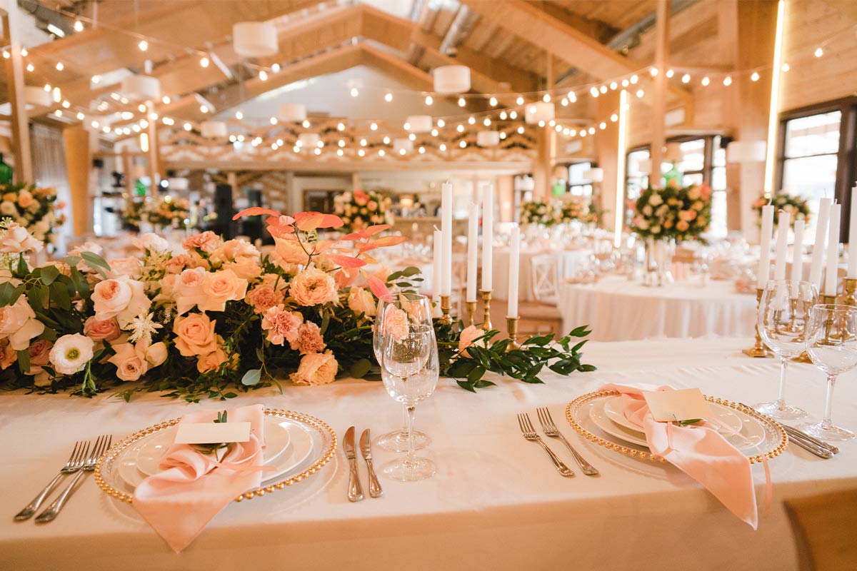 Wedding venue with pink flowers and candles on tables with table settings and string lights in the background casting a pink glow.