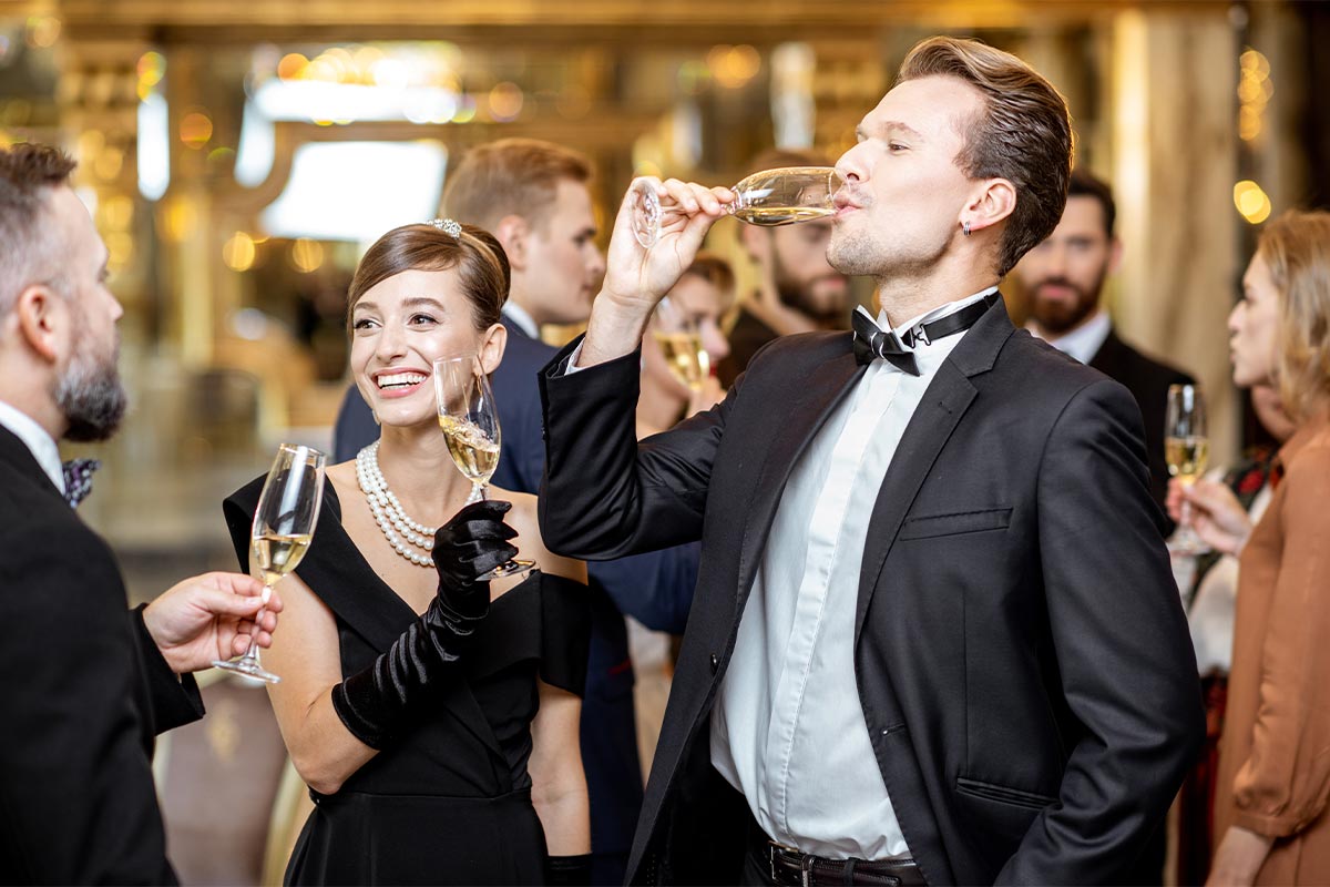 Three white friends in their 30s at a formal event dressed in formal evening wear drinking and cheering champagne in flutes