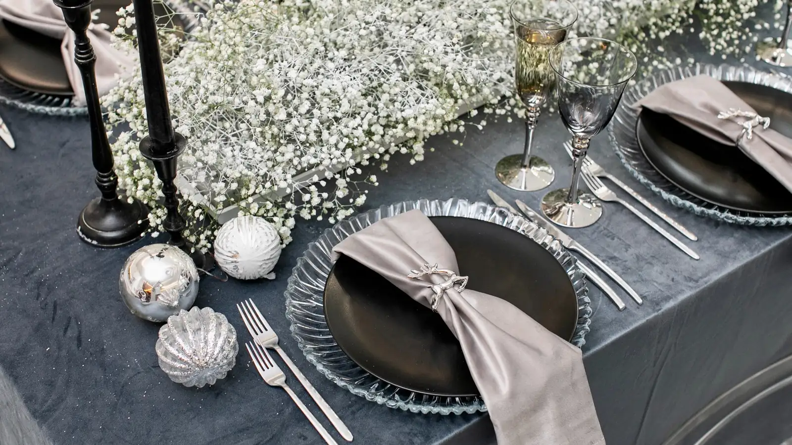 Elegant silver themed table setting with black plates, gray napkins, candles, and baby’s breath for a 25th wedding anniversary party