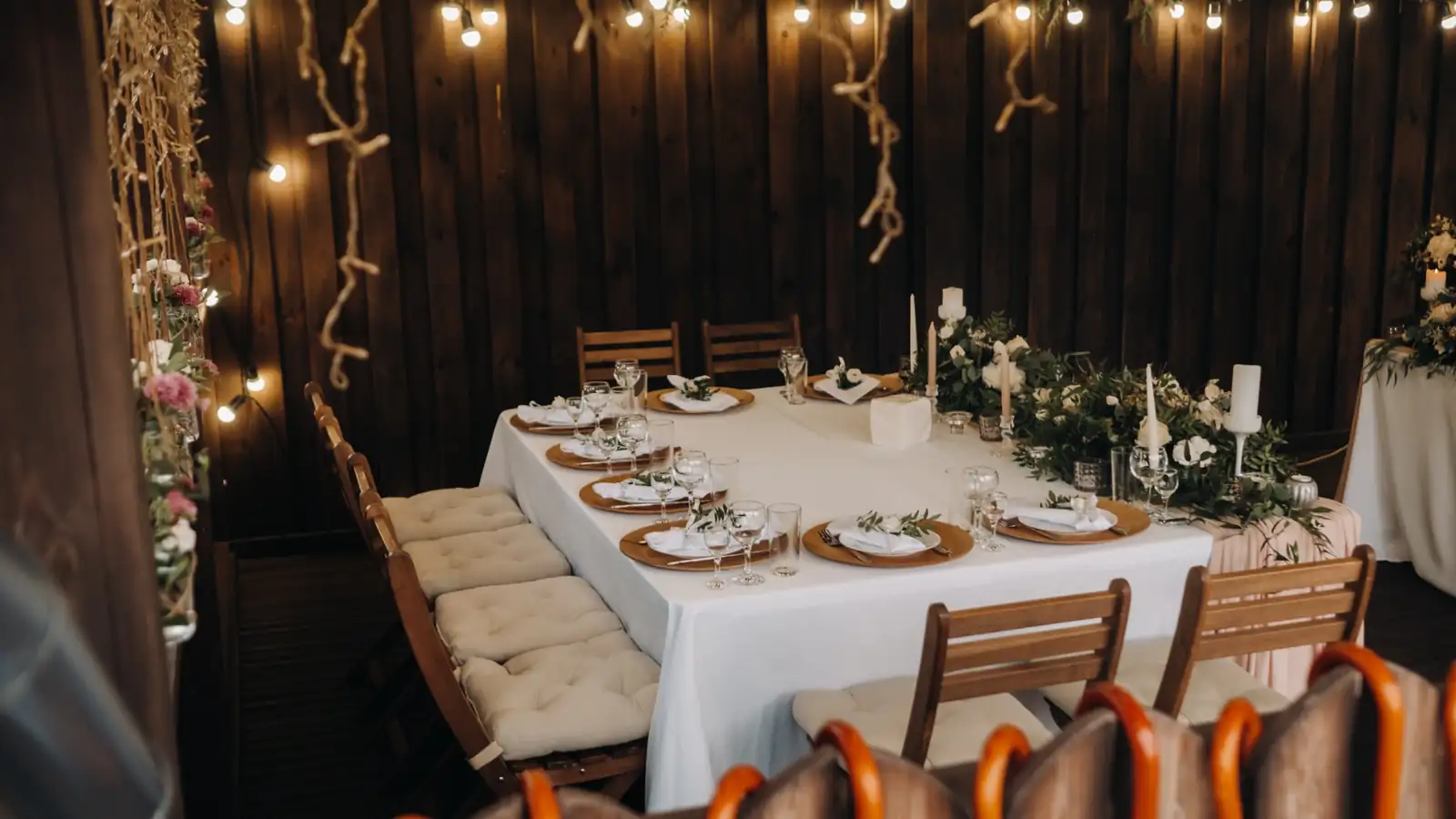 Backyard party table set for an outdoor dinner with string lights, greenery, and candles