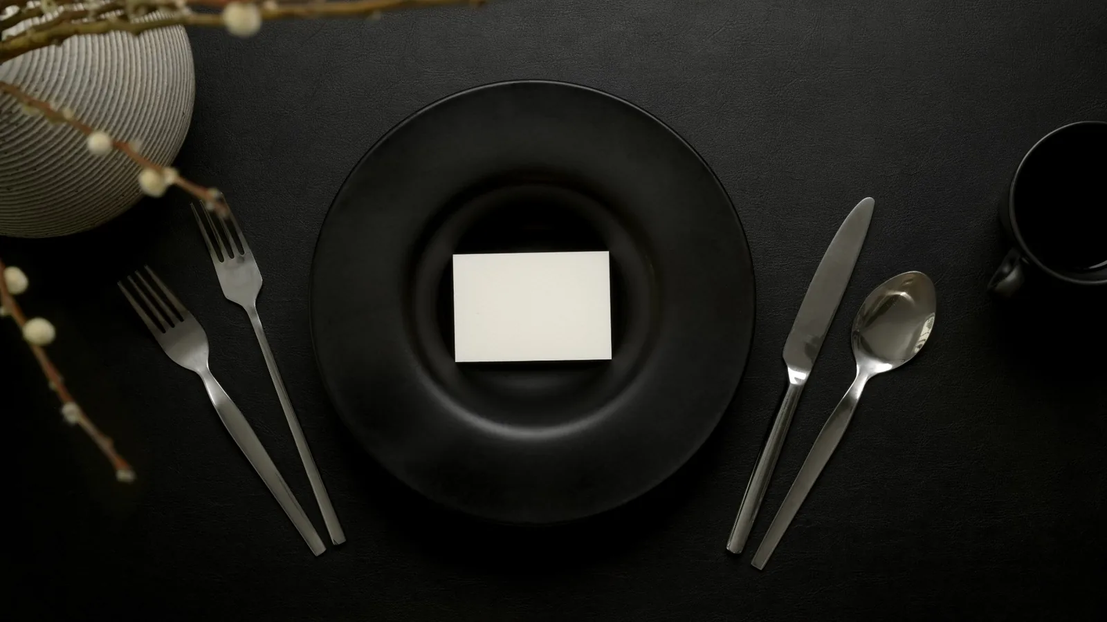 Minimal black color party table setting with matte black plate, modern flatware, and elegant dark styling