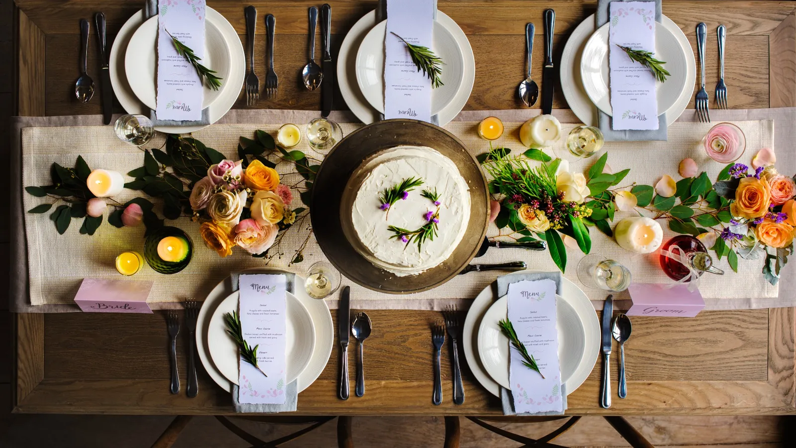 Overhead view of an elegant dinner party table with floral arrangements, candles, place settings, and a cake centerpiece