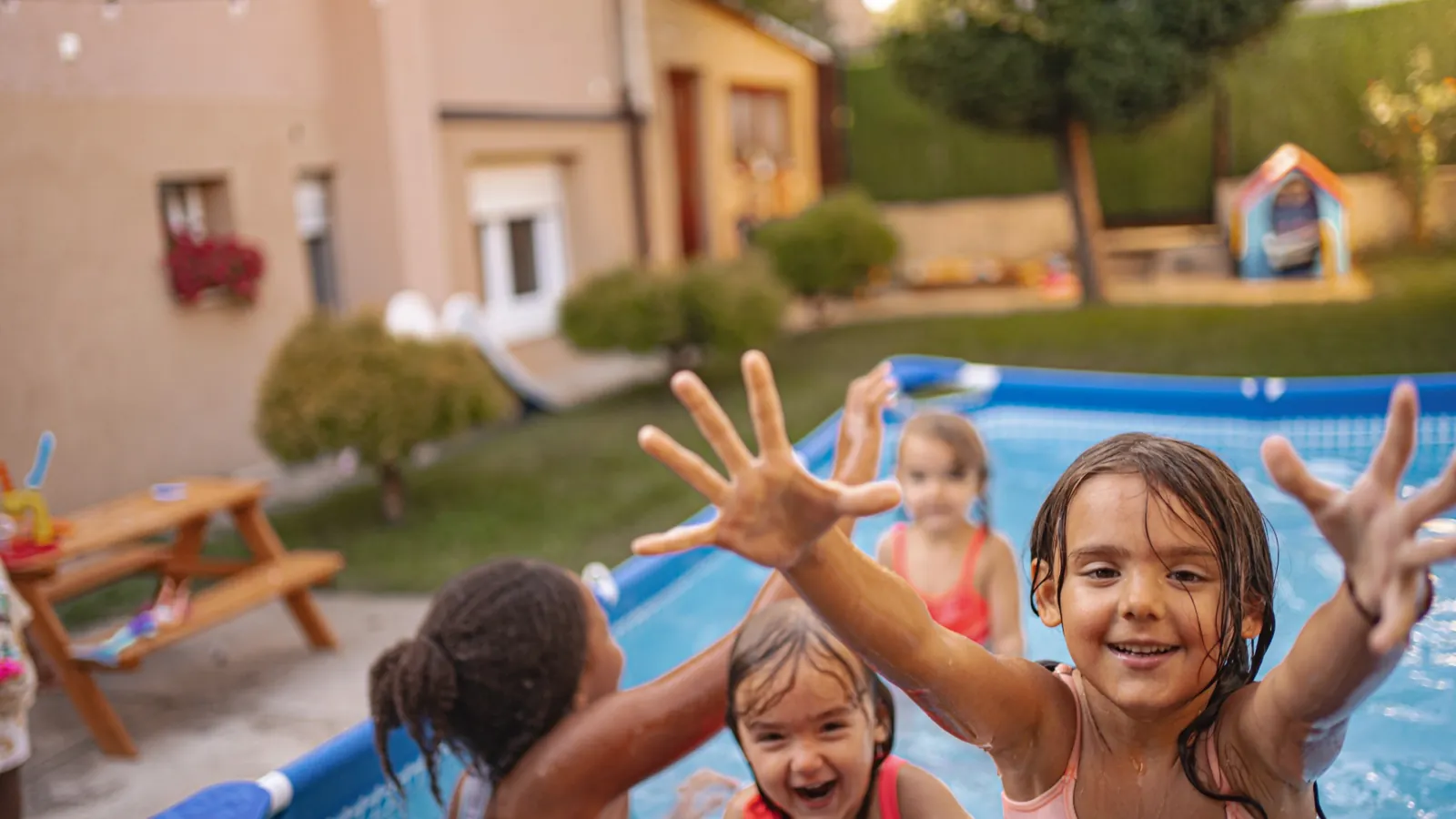 Kids playing and splashing in a backyard pool during a fun summer party with a house and yard in the background