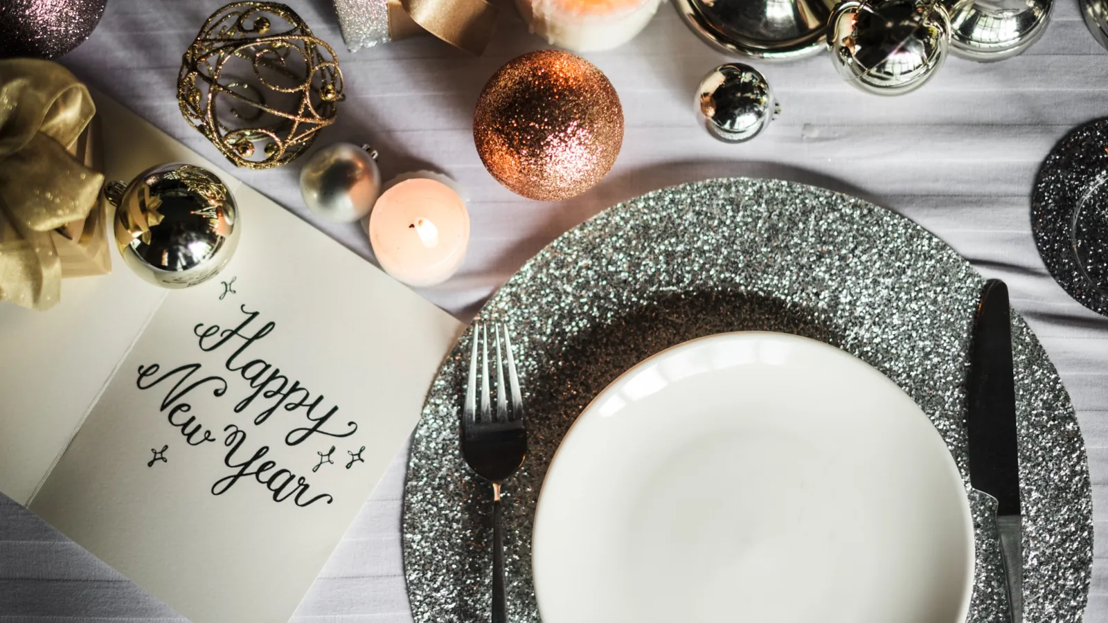 New Year’s Eve dinner table setup with sparkling decorations, candles, and a plate setting next to a card that reads happy new year