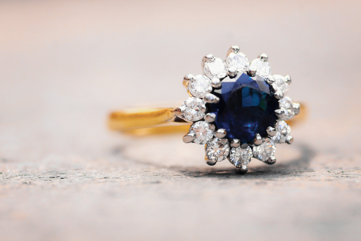 Woman’s engagement ring with a big blue sapphire, surrounded by diamonds on a gold band