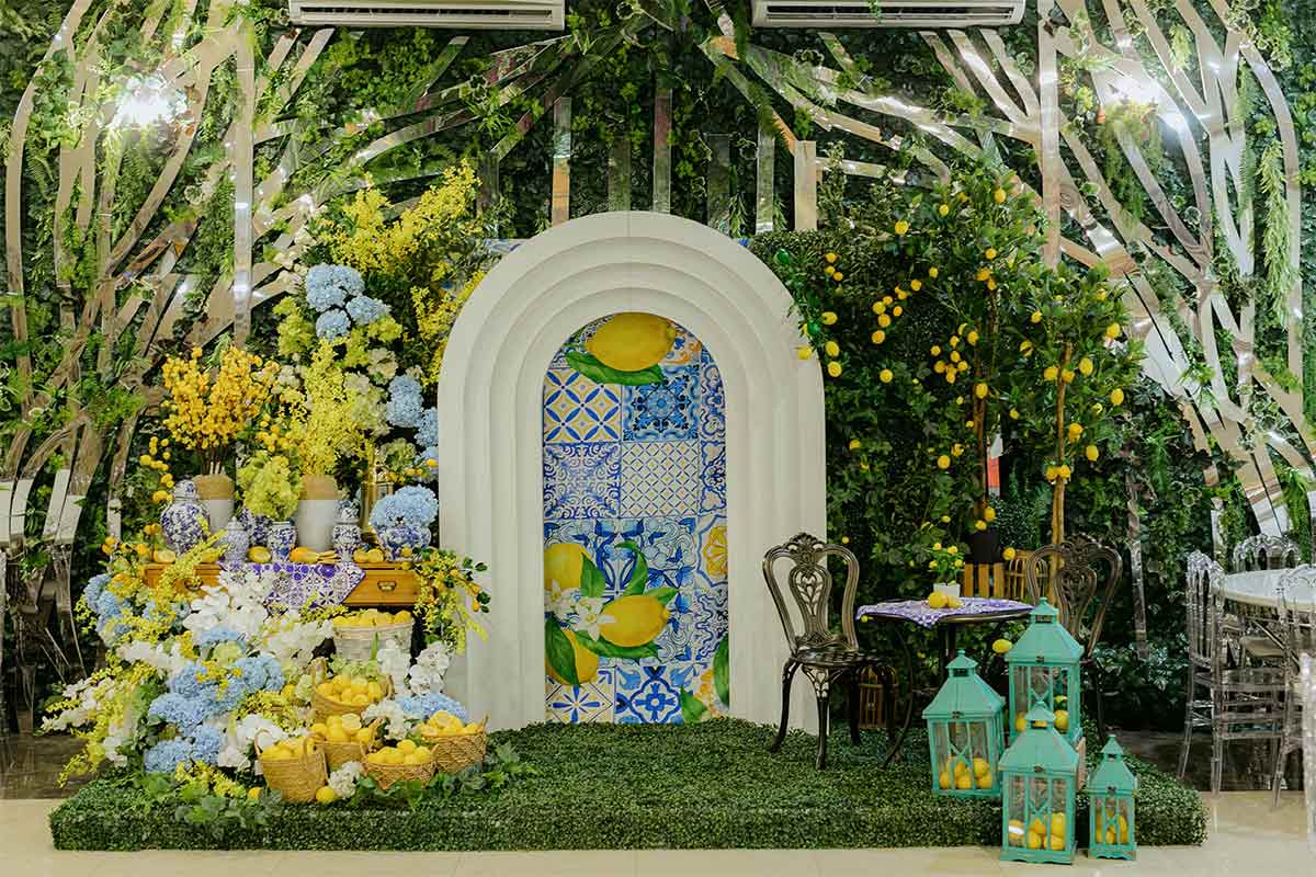 A white archway decorated with lemons and flowers next to tables and chairs in an indoor garden