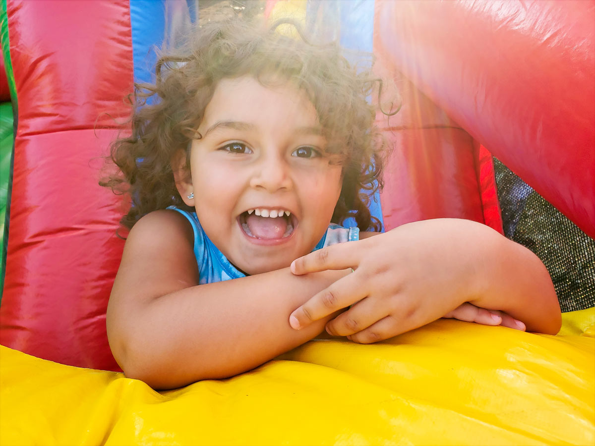  Hispanic little girl laying down on a bouncy house and smiling at the camera