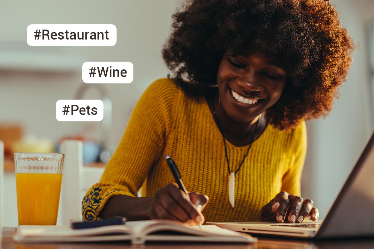 black 30 something female in yellow shirt smiles while she writes in a notebook on a table next to a glass of orange juice