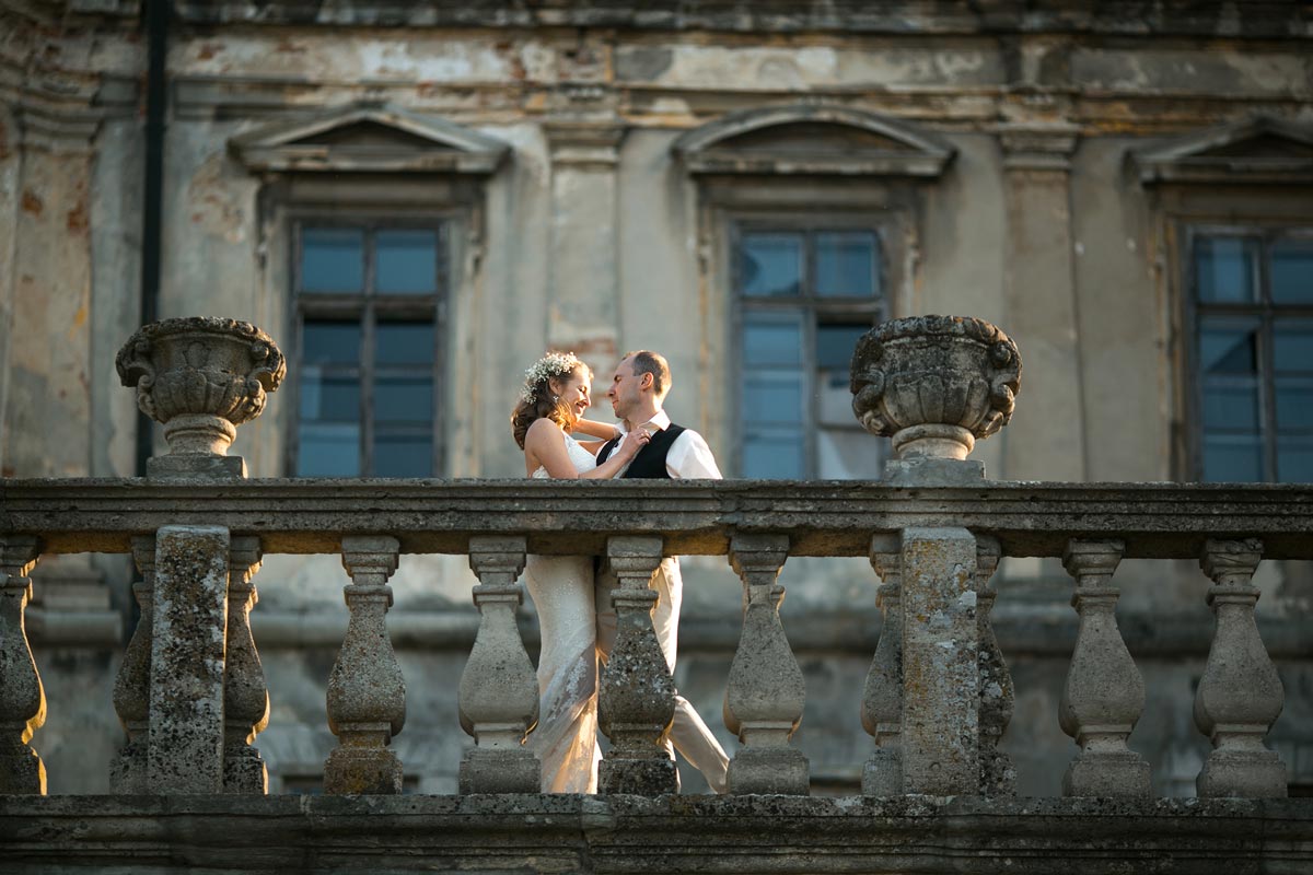 40 something white couple posing together outdoors on castle balcony in wedding dress and suit