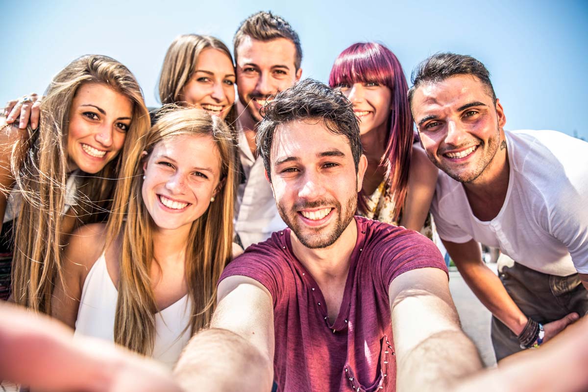  A man takes a selfie photo with a group of 6 other smiling people.