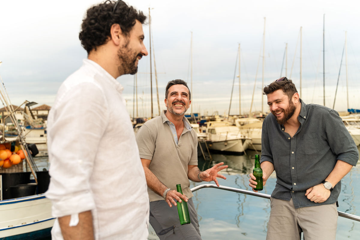 Three 35-year-old men laughing and talking on a boat while enjoying some beers.