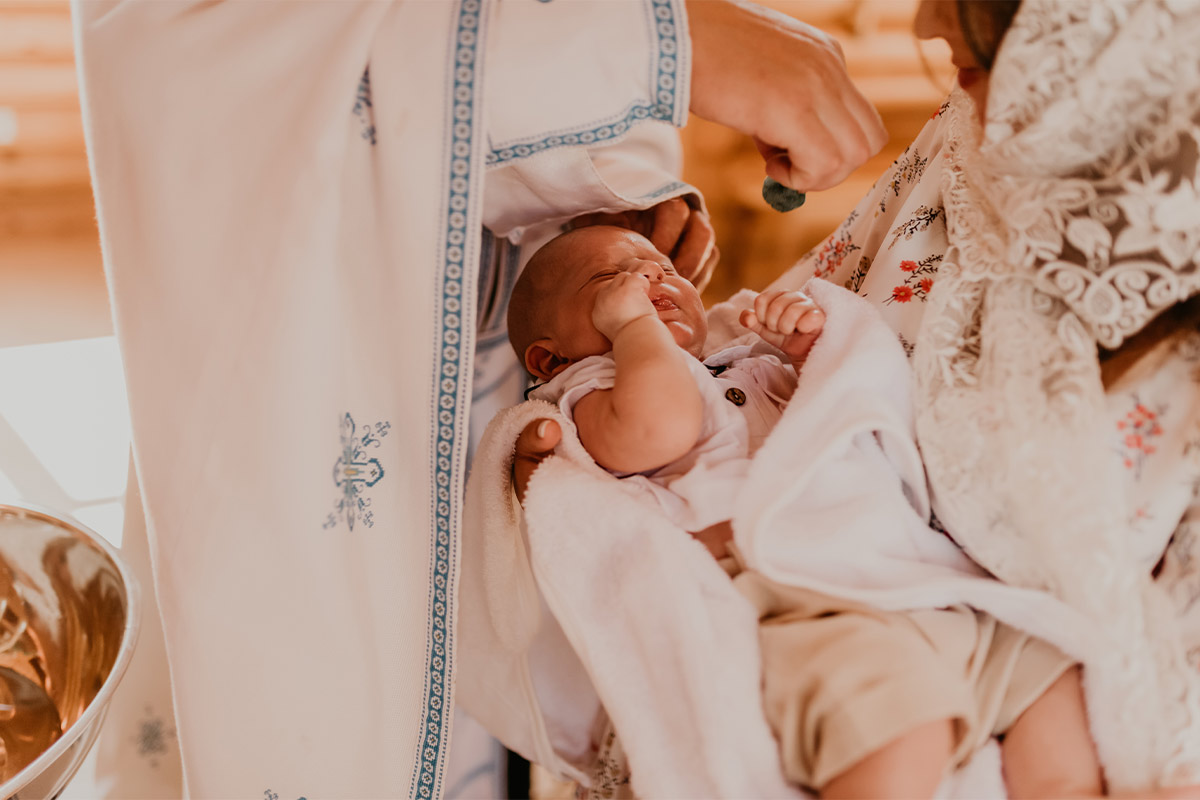 A white newborn baby in their mothers arms wrapped in blankets, while receiving a blessing. 