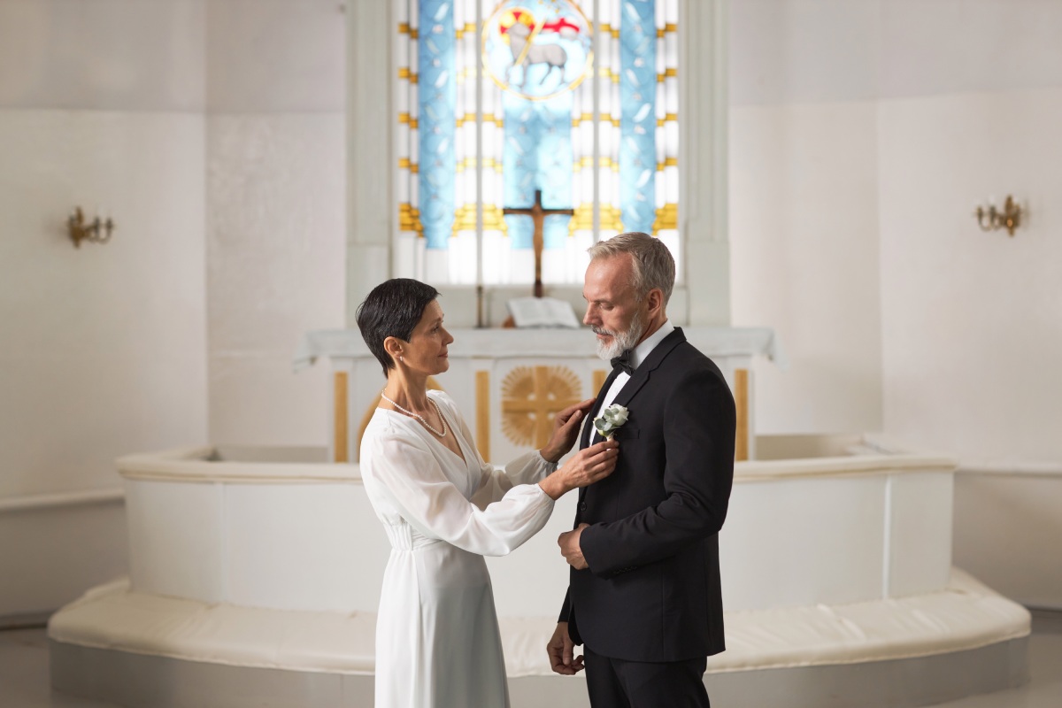 An older white bride and groom stand in front of the altar at a church