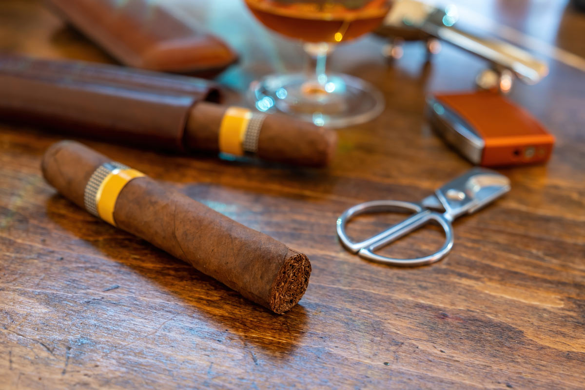 Cigars and accessories on a table with a drink blurred out in the background.