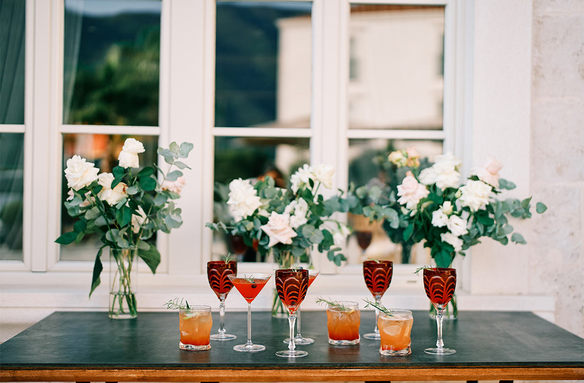 Glasses with alcoholic drinks arranged on a table with flowers behind