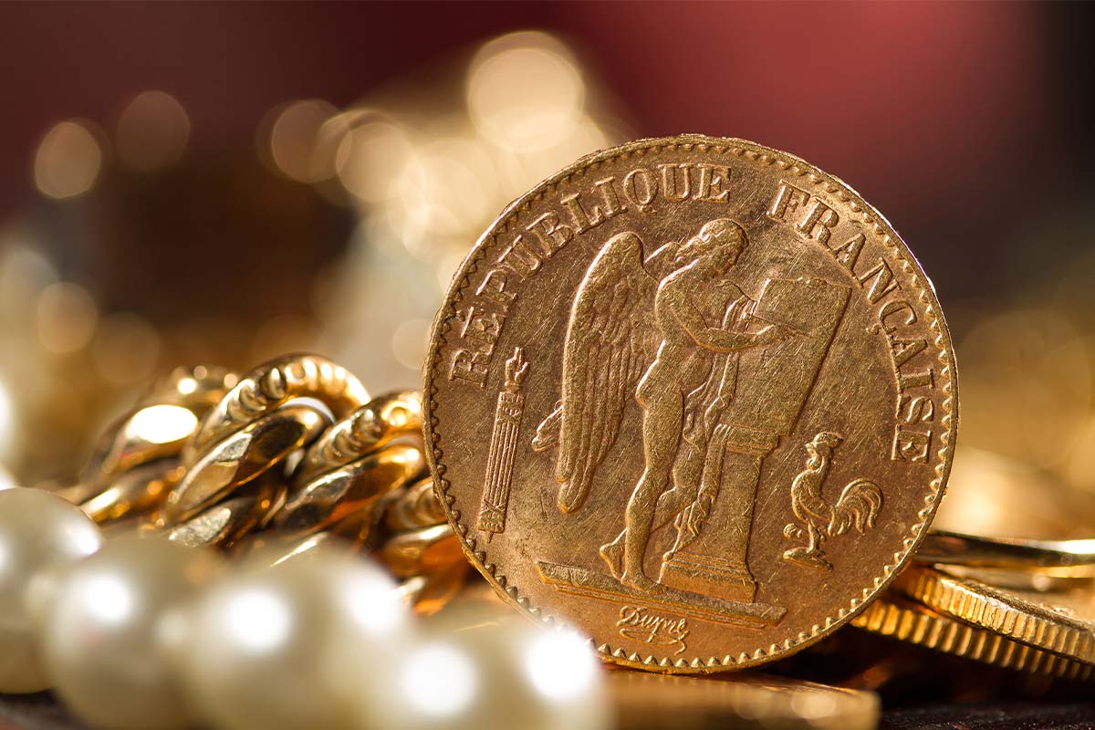 Up close photo of fancy, gold coin with gold coins and jewelry blurred in the background