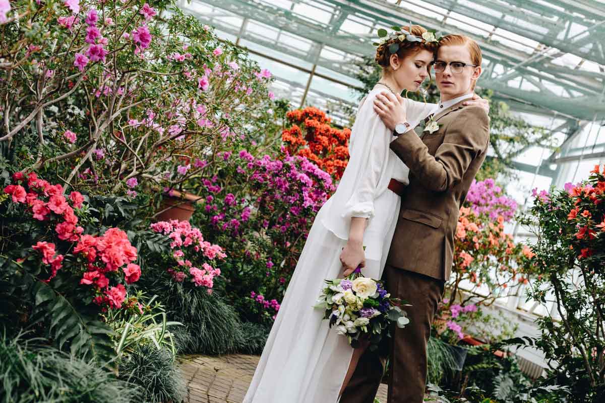 White 30 something wedding couple with bouquet in a scenic garden, surrounded by flowers