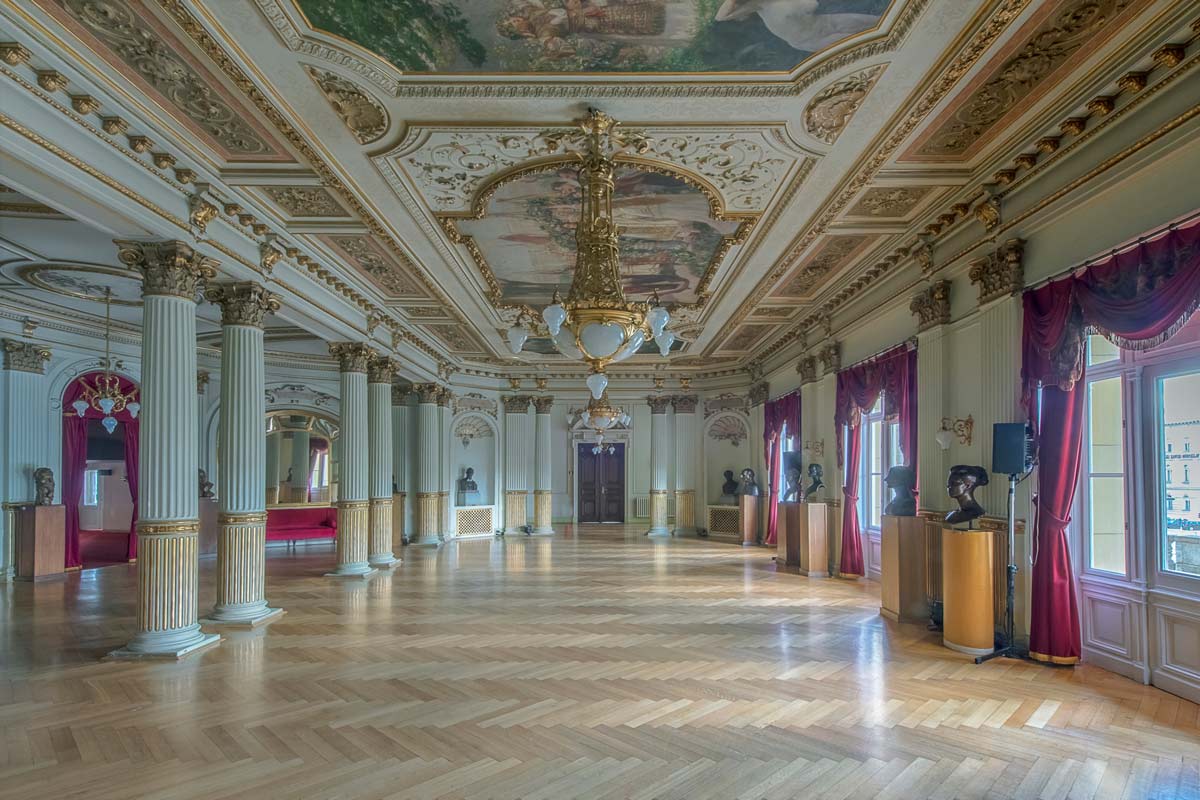 Shot of the inside of the Croatian National Theater featuring traditional European art, murals, and gold chandeliers and pillars