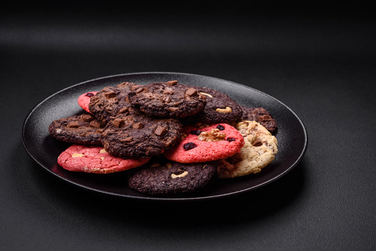 Assortment of chocolate and pink colored cookies on a black plate on a black table. 