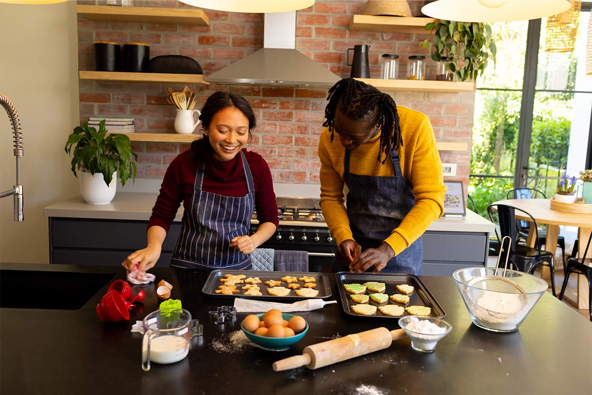 Happy diverse 20 something couple in aprons preparing Christmas cookies together