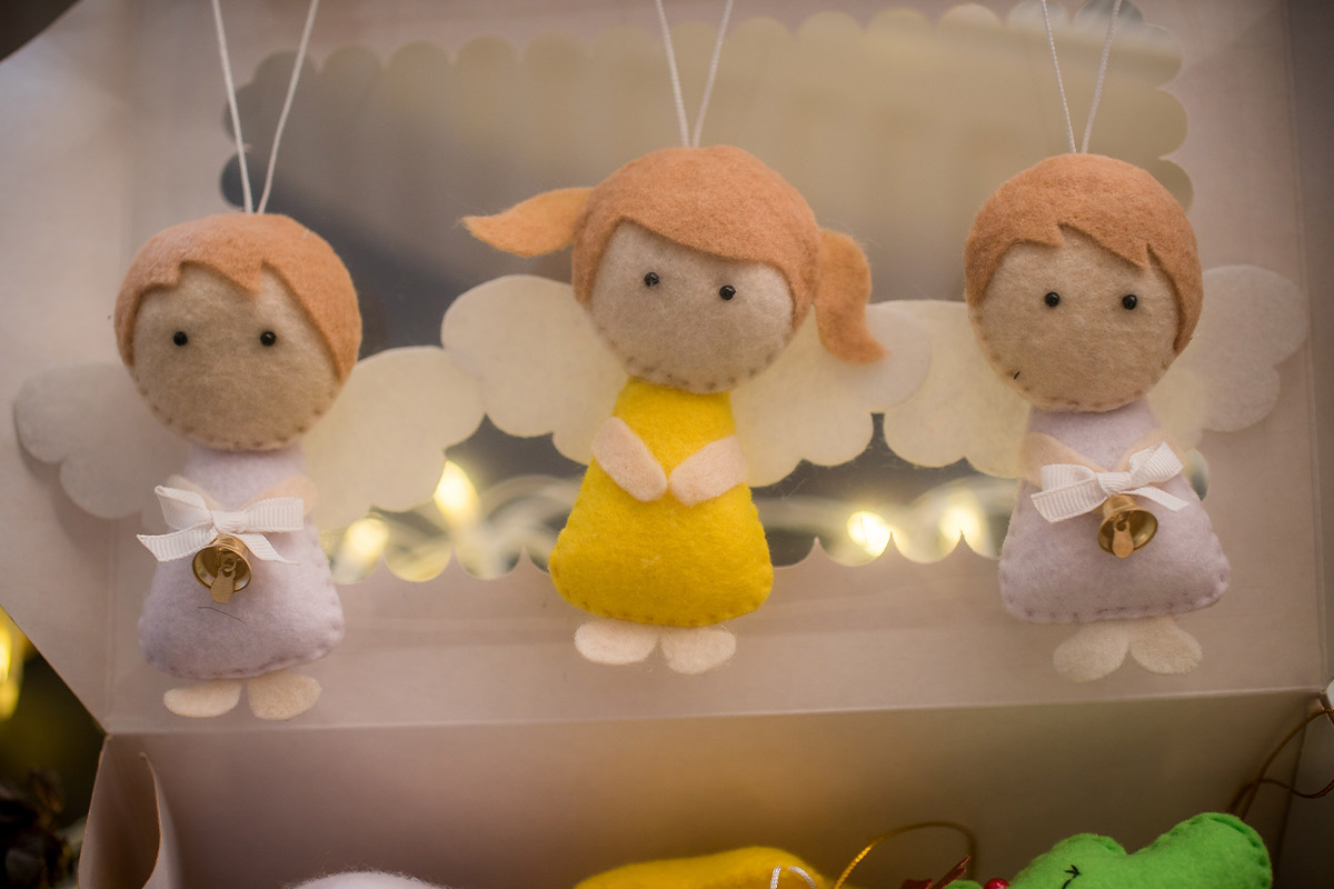 three felt angles on string with orange hair, the middle one in pigtails and a yellow dress, and the two on the side with short hair in pink dresses with bells