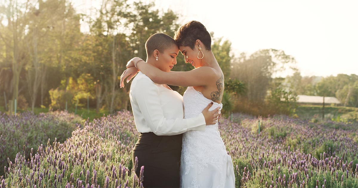 30 something mixed race lesbian couple dressed in white hug and lean their heads together in a sunny lavender field 