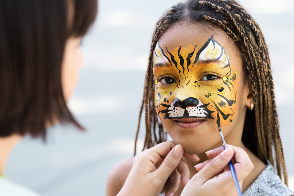 Black 10 year old girl getting her face painted like a tiger by a professional artist.