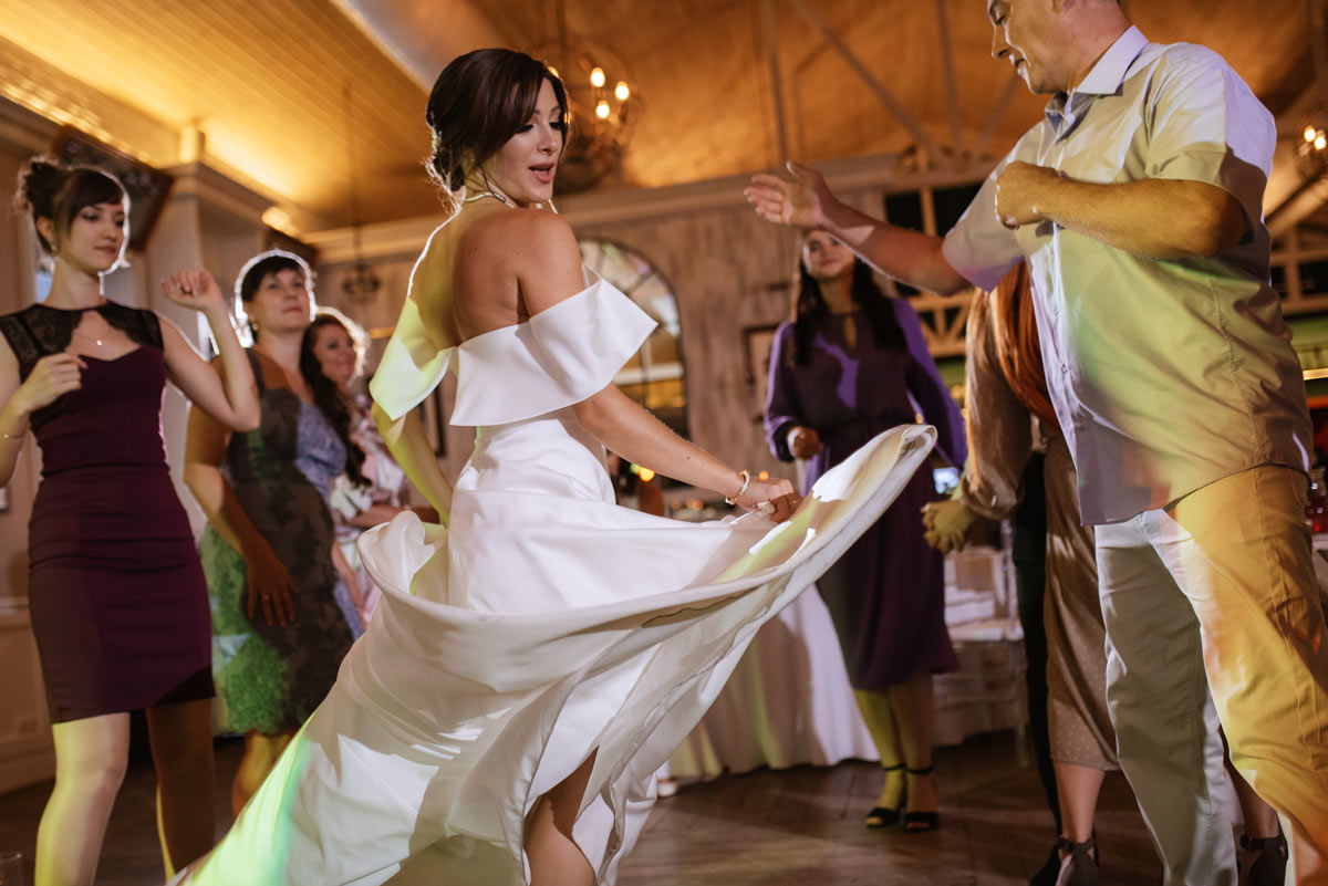 Brunette bride lively dancing with father as guests surround the dance floor