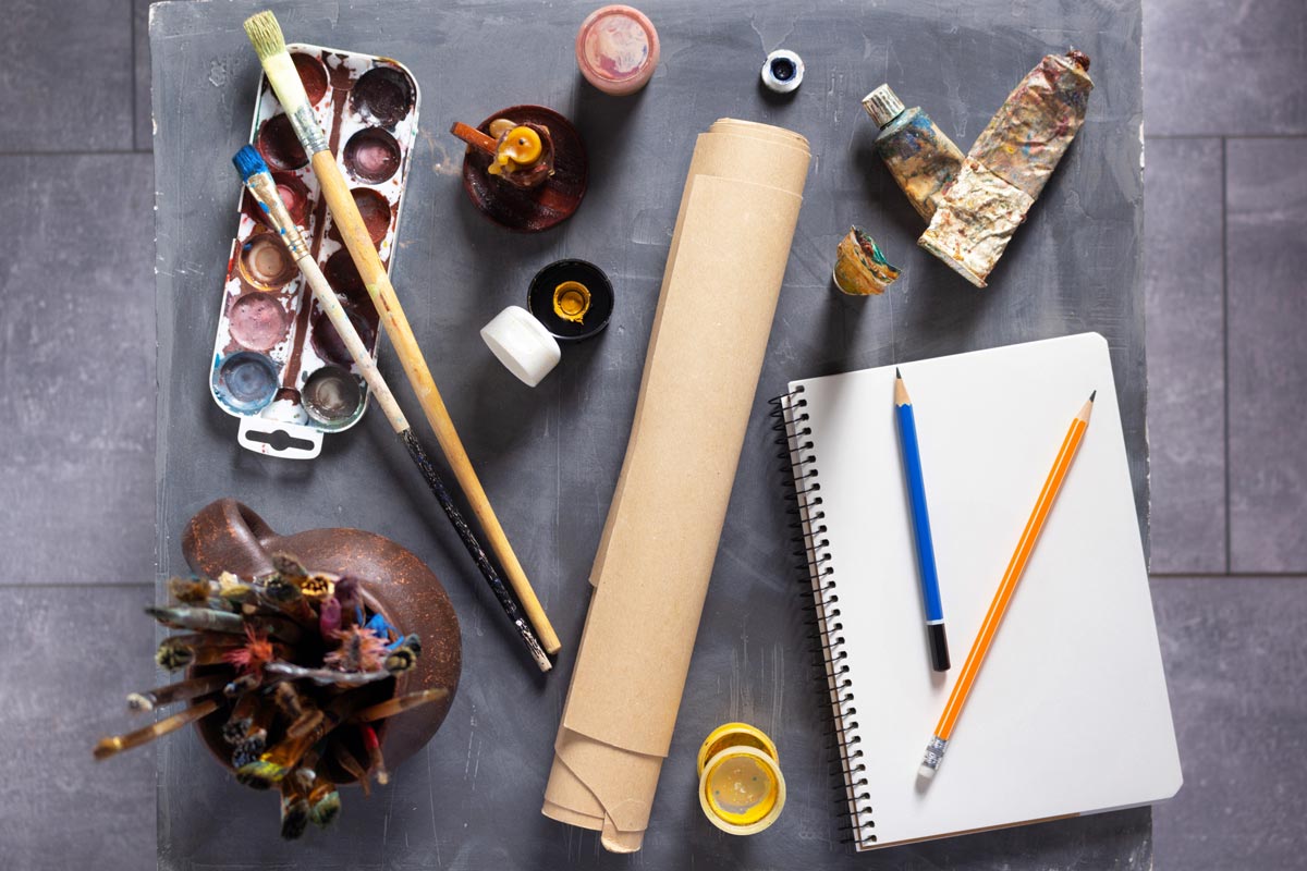 overhead view on paint, paint brushes, sketch pad, and other paint supplies. 