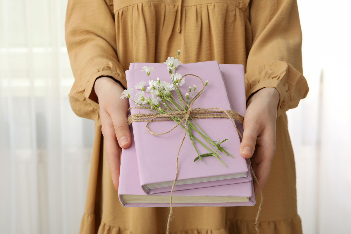 Woman holding out two pink books wrapped in ribbon and flowers. 