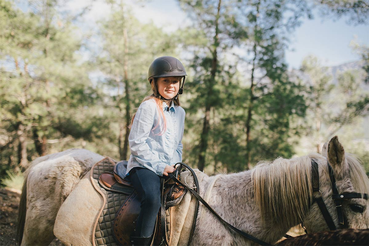 Little white girl sitting on a horse in the woods taking a lesson 