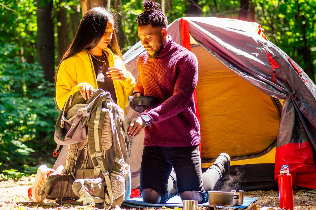 Woman and man looking through backpack while camping in the woods. 