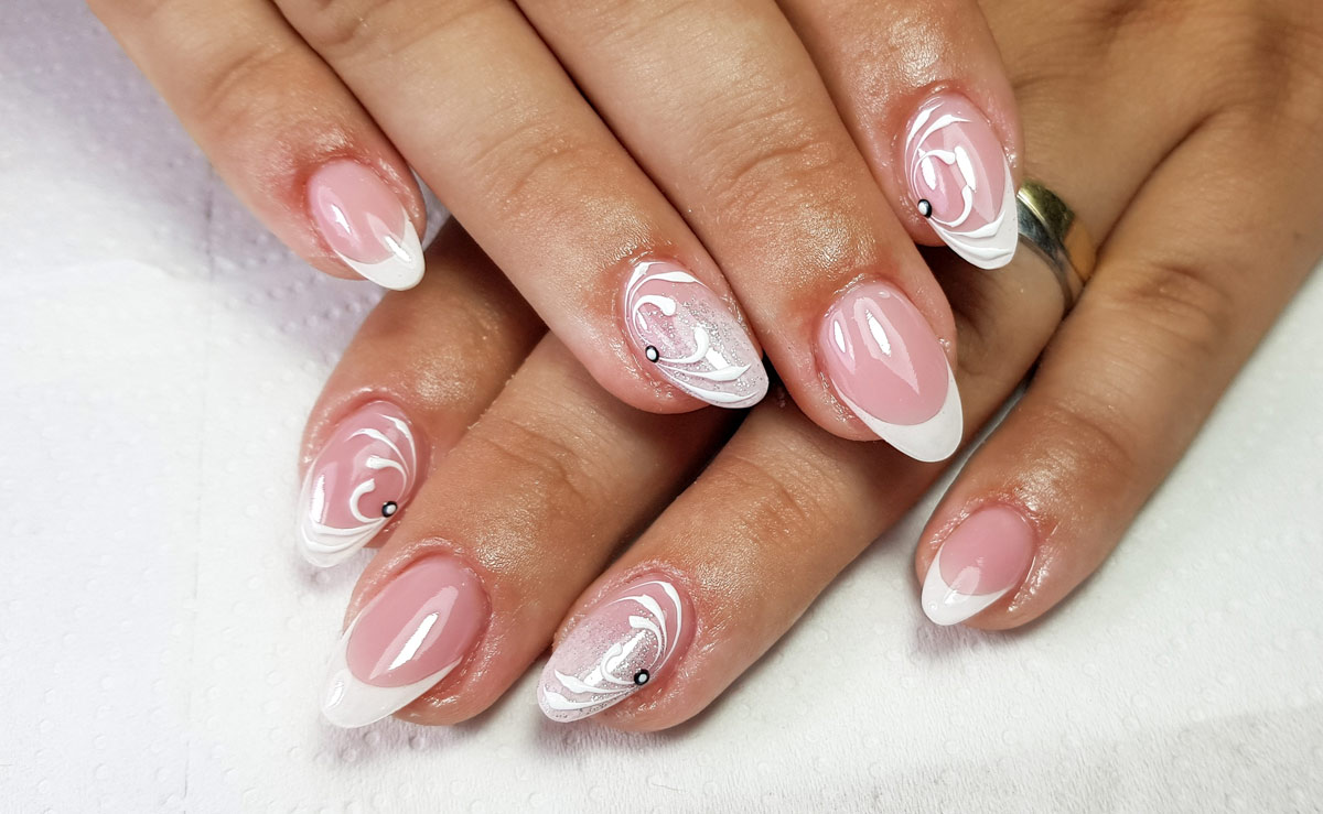 Close-up of a woman’s hands with a classic white French manicure on oval-shaped nails featuring simple white and silver nail art accents.