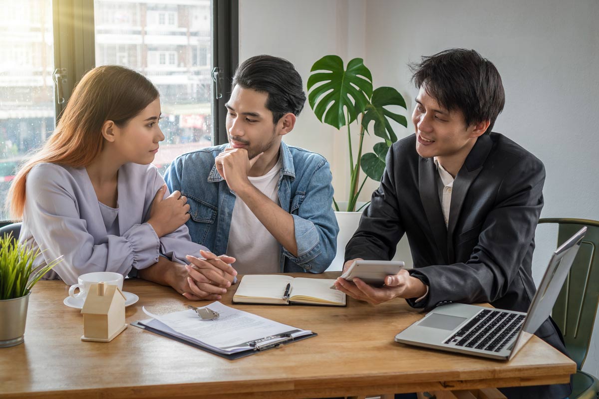 White couple in their 30s meeting with an Asian financial advisor in his 40s at a desk to discuss loan options.