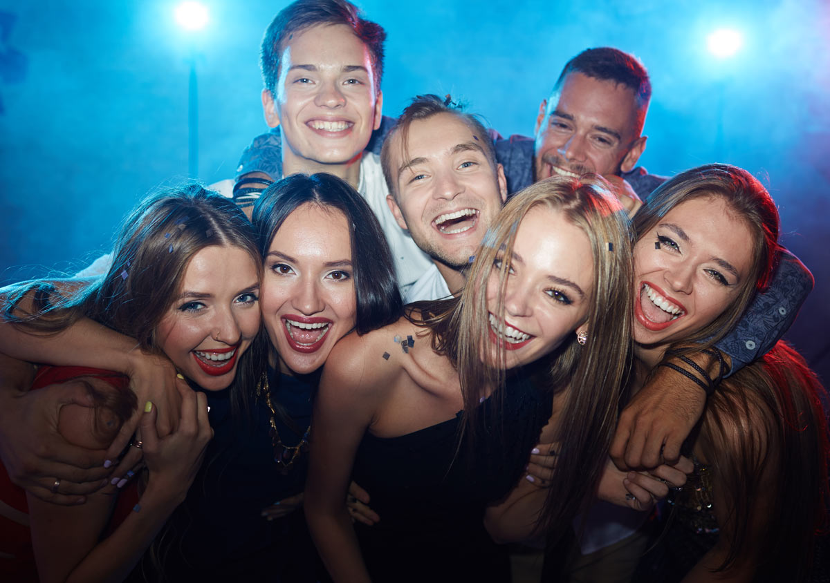 Group of white 21-year-old4 women and 3 men having their arms around each other while taking a group picture outside of a party.