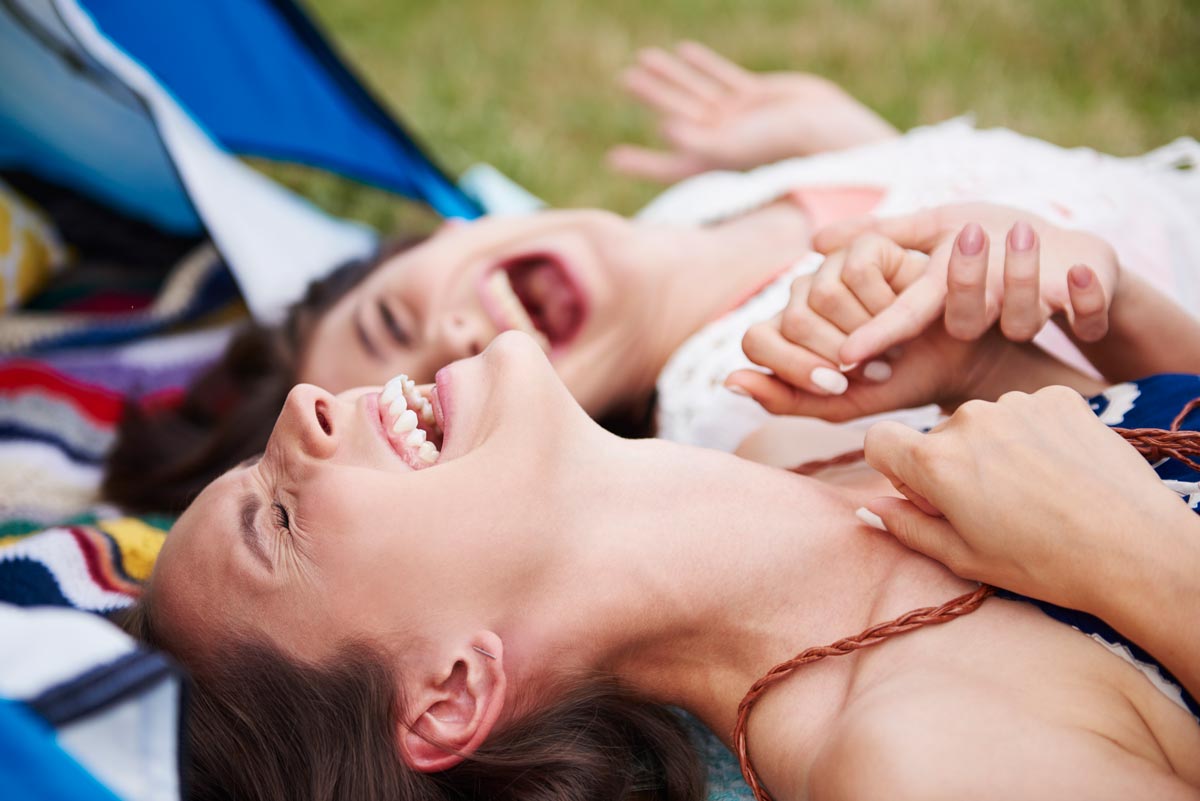 Two young white girls laying in the grass on a blanket laughing 