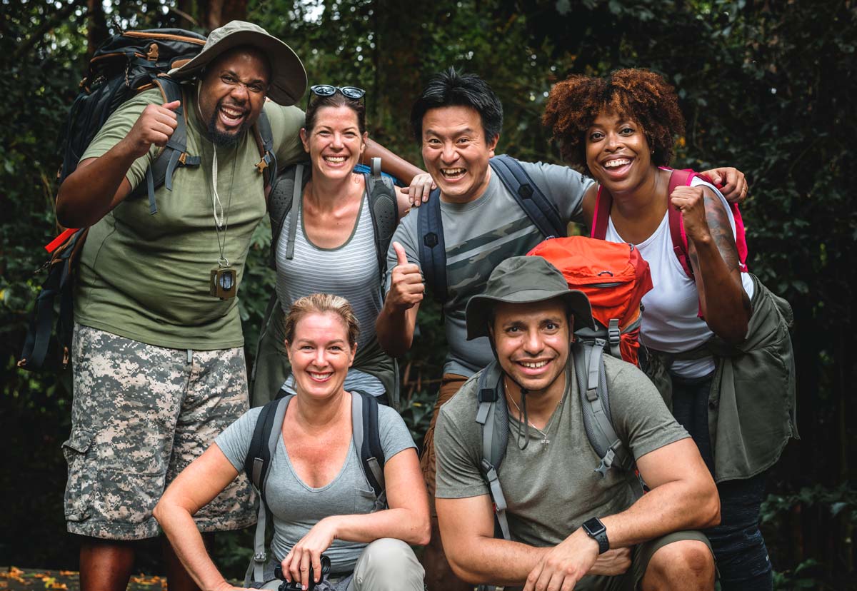 Group of 30 something friends in hiking gear smiling and and giving thumbs up to the camera