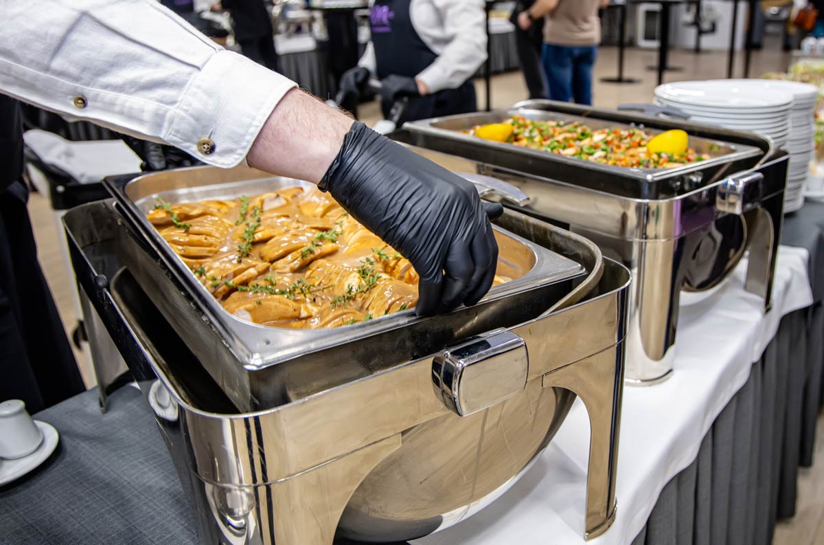 Close up of caterers in black disposable gloves setup hot food trays in chafing dishes to keep food warm at a luxury event.