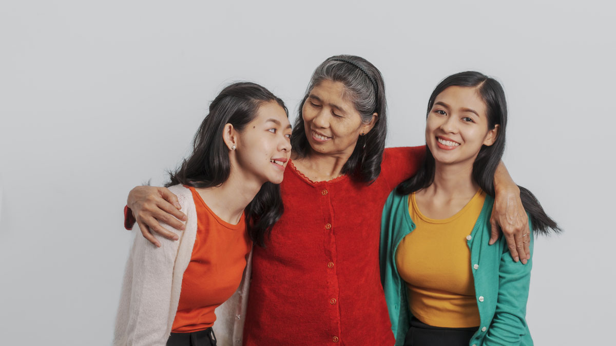 An Asian 60-year-old woman with her arms around an Asian 15-year-old girl and an Asian 20-year-old woman’s shoulders.