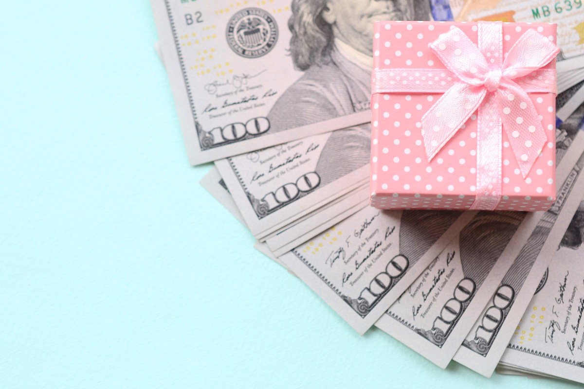 pink polka dot gift box sits on top of laid out 100 dollar bills against a light blue background